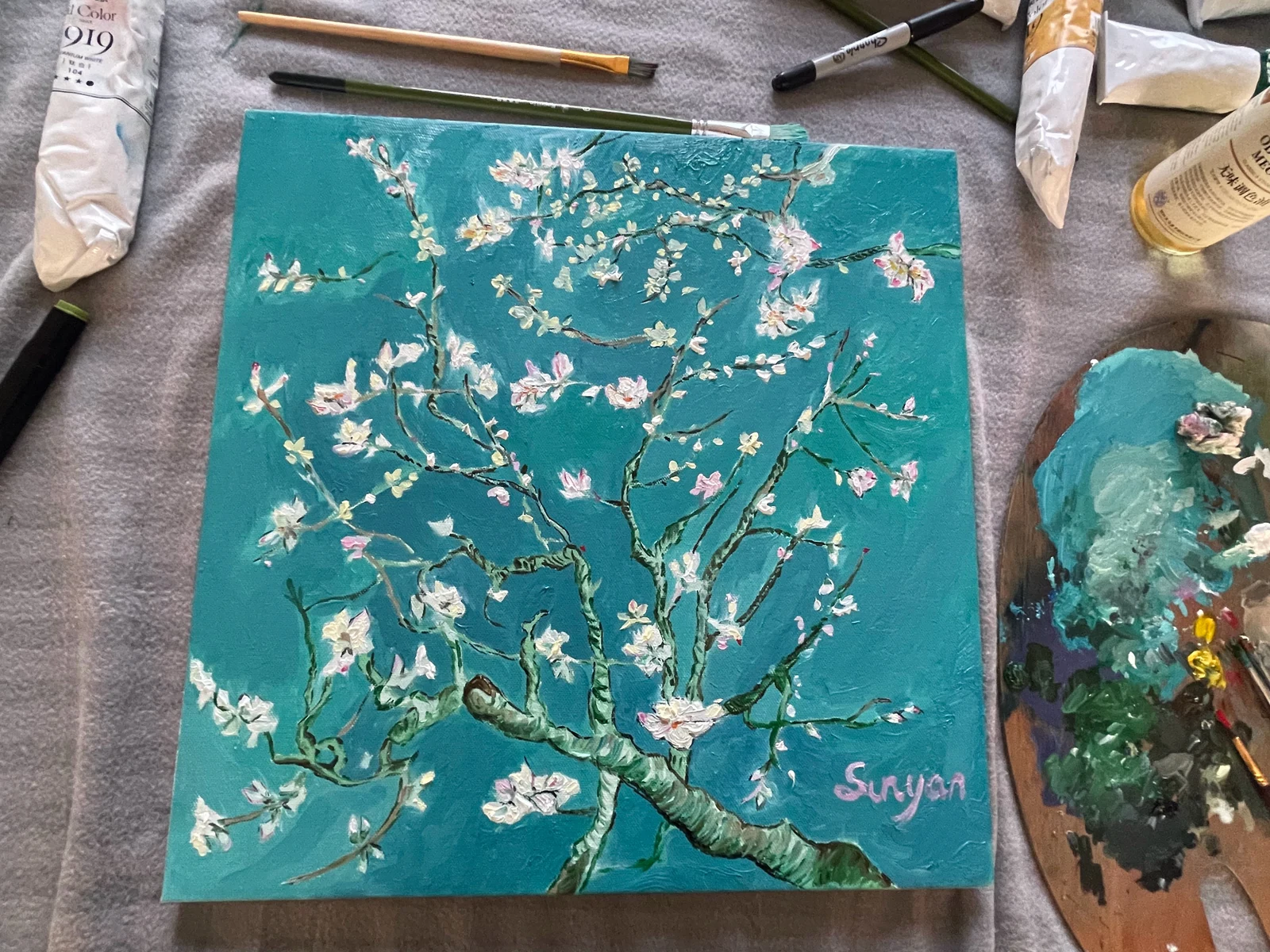 White almond blossoms against turquoise on a canvas, with brushes and a palette beside it